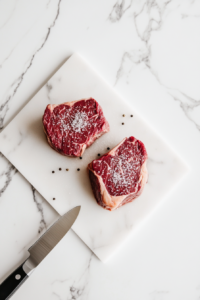 This image shows filet mignon steaks being seasoned generously with salt and pepper on a cutting board, ready to be seared for the classic steak marsala dish.