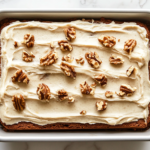A perfectly sliced piece of banana cake with creamy frosting and chopped walnuts on top, showcasing the moist texture and delicious layers of the homemade dessert.