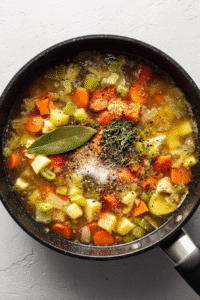 Add chicken broth, salt, garlic powder, thyme, paprika, pepper, and a bay leaf. Let it all come to a lively boil.