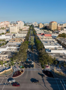 miracle_mile_drone_view.jpg Aerial view of Miracle Mile in Coral Gables, showcasing vibrant streets lined with shops and trees under a clear blue sky.