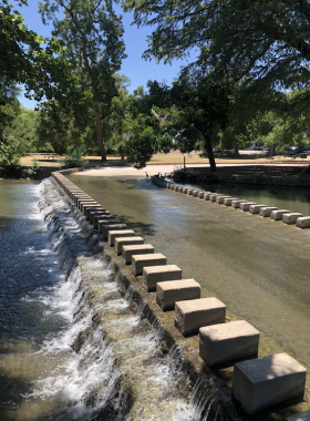 Rustic stone bridge crossing a gentle rive An old stone bridge with arched spans crosses a calm river, surrounded by trees. The bridge’s historic design blends harmoniously with the natural scenery, offering a tranquil, timeless view.
