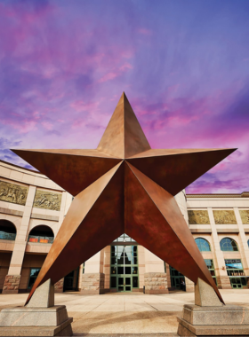 Exterior view of the Bullock Texas State History Museum: A stunning view of the Bullock Texas State History Museum, showcasing its modern architecture with large glass windows and a unique roof design. The entrance is adorned with Texas flags, inviting visitors to explore the state's rich history.