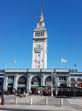 Ferry_Building_Marketplace.jpg A vibrant scene of the Ferry Building Marketplace bustling with people shopping and dining. The iconic clock tower stands tall against the backdrop of a clear sky, while vendors display fresh produce and artisanal goods.