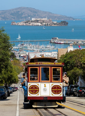 Cable_Car_and_Alcatraz.jpg A classic San Francisco cable car traveling along a steep street, with Alcatraz Island visible in the distance. The vibrant red and gold of the cable car contrasts with the blue waters of the bay, encapsulating the charm of the city.