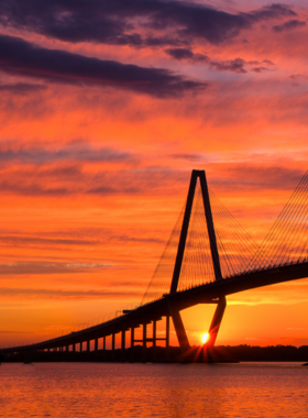 Charleston_Sunset_Fishing_Boat.jpg A serene sunset over the Charleston harbor, featuring a silhouetted fishing boat gently bobbing on the calm waters. The sky is ablaze with warm colors, including deep oranges, soft pinks, and golden yellows, creating a stunning backdrop for this tranquil scene. The reflection of the vibrant sky on the water enhances the beauty of the moment, embodying the peacefulness of a day ending in Charleston.