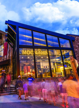 Sugarlands Distilling Company An inviting interior of Sugarlands Distilling Company, showcasing the distilling process with shiny copper stills and barrels. The atmosphere is lively, with visitors sampling various flavors of moonshine and spirits.