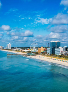 Myrtle_Beach_Promenade A scenic view of Myrtle Beach's promenade, showing the beautiful shoreline with clear blue waters and tourists enjoying the sun and sand. The beach offers a relaxed atmosphere with plenty of activities.