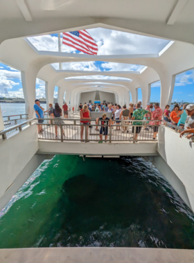 USS Arizona Memorial at Pearl Harbor This image shows the USS Arizona Memorial at Pearl Harbor, a solemn site surrounded by clear blue water, with visitors paying their respects. The white structure stands as a tribute to those who lost their lives during the attack on December 7, 1941.