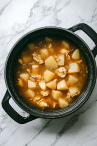 A simmering pot filled with diced potatoes, fresh corn, and whole chicken breasts fully submerged in broth.