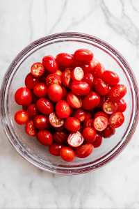 Halve the grape tomatoes and add them to a large mixing bowl.