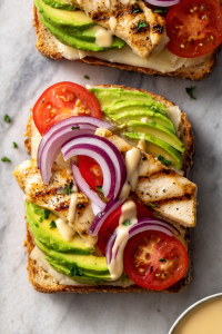 On the unbuttered side, spread the mayo-mustard mix. Layer chicken, avocado slices, cheese, tomato, and red onion.