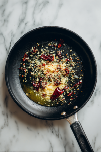 Add cumin seeds, garlic, dry red chilies, hing, and chili powder. Sauté until aromatic.