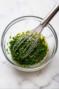 In a mixing bowl, combine parsley, garlic, olive oil, red wine vinegar, oregano, salt, black pepper, and red pepper flakes. Stir to blend.