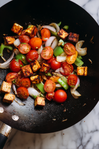 In a separate pan, stir-fry onion, capsicum, tomato, and paneer cubes until lightly roasted.